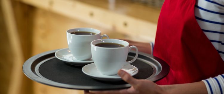 Eine Servicekraft serviert zwei Tassen Kaffee auf einem Tablett