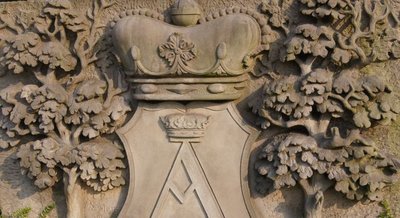 Der Wappenstein vor dem Rathaus. Das Wappen der Stadt zeigt zwischen zwei Bäumen einen gekrönten Schild. Darin ein gotisches großes A. 