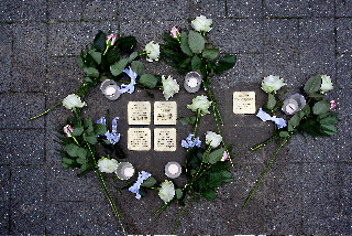 Stolpersteine umgeben von Rosen und Kerzen