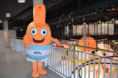Maskottchen Ezzy des Energie-Erlebnis-Zentrums steht an einem Geländer