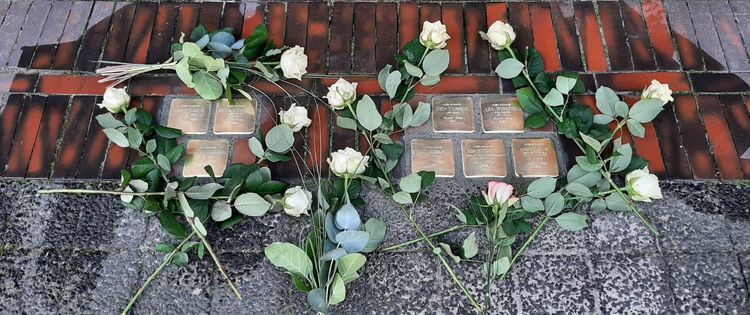 Im Straßenpflaster verlegte Stolpersteine, ringsum weiße Rosen  