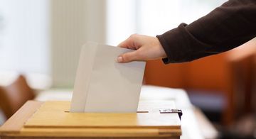 Eine Person wirft einen Stimmzettel in eine Wahlurne