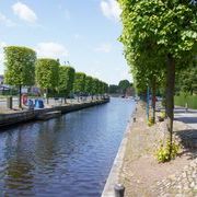 Der Auricher Hafen von der Julianenburger Straße aus gesehen. Mittig verläuft der Kanal. Rechts und links ist er von Bäumen umsäumt. 