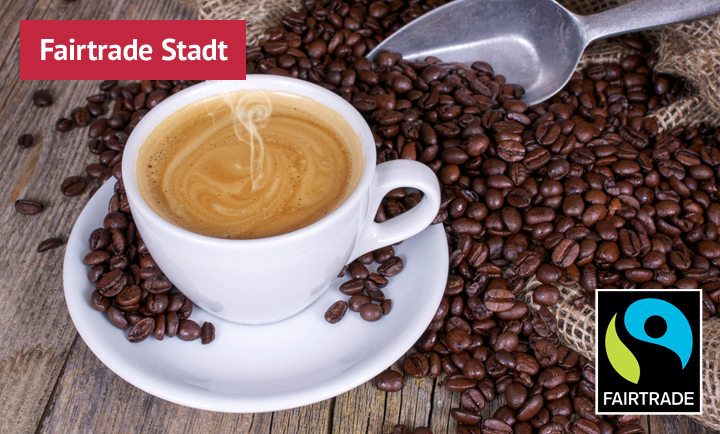 Eine Tasse mit Kaffee gefüllt. Rings herum liegen Kaffeebohnen. Das Fairtrade-Logo ist abgebildet.