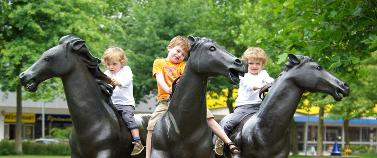 Drei Kinder sitzen auf drei Pferdeskulpturen 
