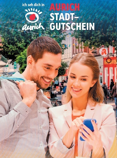 Werbeplakat Stadtgutschein Aurich. Zwei Personen halten sich in der Fußgängerzone auf. Eine Person bedient ein Handy, die andere Person schaut zu. 